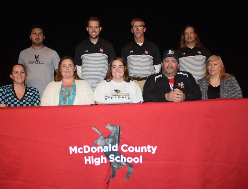 RICK PECK/SPECIAL TO MCDONALD COUNTY PRESS Whitney Kinser (bottom, center) is flanked by her mom and dad (Valerie and Bronnie Kinser) at a college signing ceremony held on Nov. 13 at McDonald County High School. Kinser signed a national letter of intent to play softball at Lindenwood University in St. Charles. Back row are MCHS coaches (left to right) Skyler Rawlins, Kyle Smith, Lee Smith and Heath Alumbaugh.