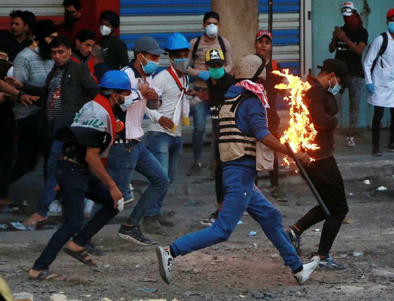 Demonstrators work Thursday to extinguish a protester who was set on fire during clashes between Iraqi security forces and anti-government protesters in Baghdad. More photos are available at arkansasonline.com/1122protests/ 