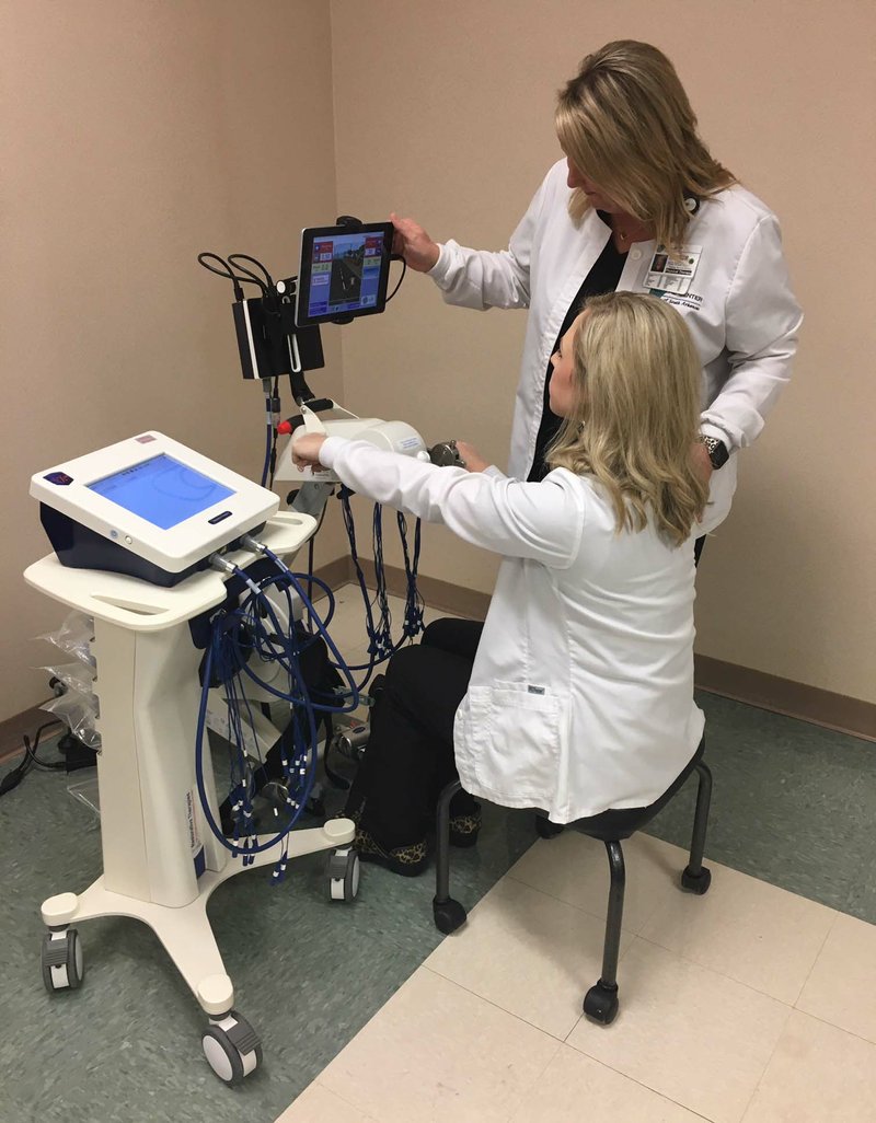 Director of therapy services Amber Steele and director of in-patient rehab Shelby Cater demonstrate the use of the RT300 machine at the Medical Center of South Arkansas. 