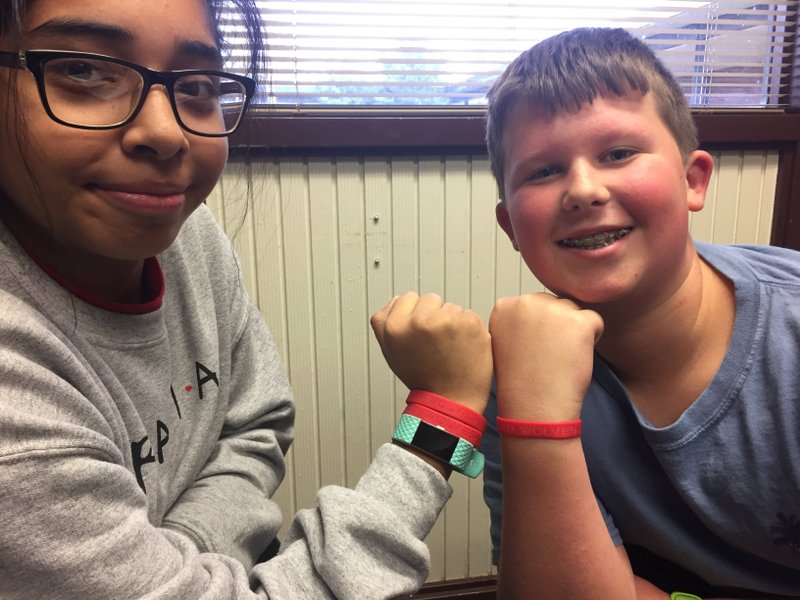 NWA Democrat-Gazette/DAVE PEROZEK Ramay Junior High School eighth-graders Cynthia Montiel and Jake Travis, both 13, show off wristbands embossed with the name of the school's new mascot -- Red Wolves -- which were handed out to Ramay students Friday.