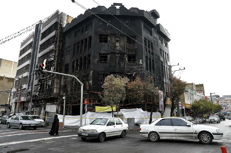 Vehicles and pedestrians last week pass a building that was set ablaze during the recent protests in Tehran, Iran.