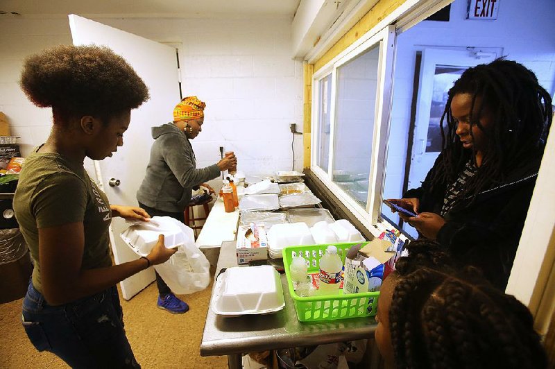 Elnora Wesley (center), owner of The House of Mental Eatery, and her 14-year-old daughter, Nadia McGhee (left), prepare orders for customers who wanted vegan Thanksgiving dishes Thursday at the food truck court on Chester Street in Little Rock. 