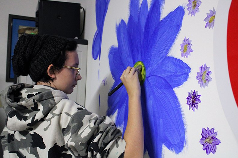 A high school student in the UCA Upward Bound program paints a flower on a wall at the Cutwell 4 Kids studio on Nov. 23. Twenty-five other students also painted on the walls that day. - Photo by Tanner Newton of The Sentinel-Record