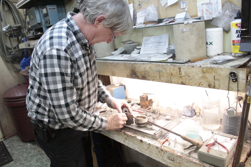 Joey Antoon demonstrates his jewelry making process. He first melts whatever metal he is using in the crucible to the right of his hands; then he pours the melted metal into the mold in his left hand. The metal is then drawn out before being shaped into its final form. 
