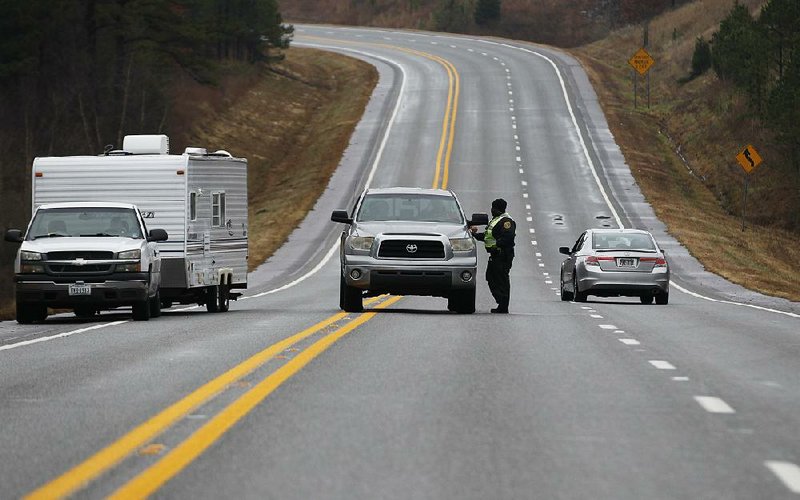 Pulaski County sheriff’s office deputy Bruce Scott notifies drivers Saturday on Arkansas 10, near where police were in a standoff with a shooting suspect, that the highway is closed. The highway reopened about noon Saturday.