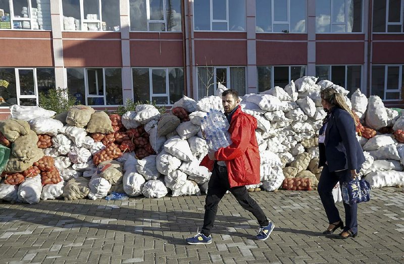 An Albanian couple carry bottled water past piles of potatoes stacked Saturday at a food collection center in Durres, which  was hit hard by last week’s earthquake. 