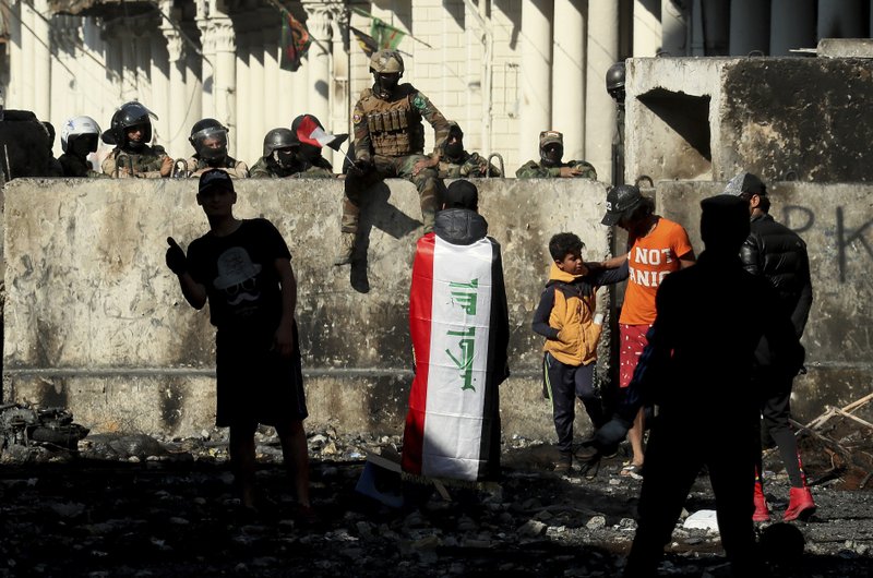 Iraqi security forces and anti-government protesters rest after both sides shake hands and converse in a rare moment of calm in hostilities called to allow time for rest after clashes in Baghdad, Iraq, Saturday. - AP Photo/Hadi Mizban