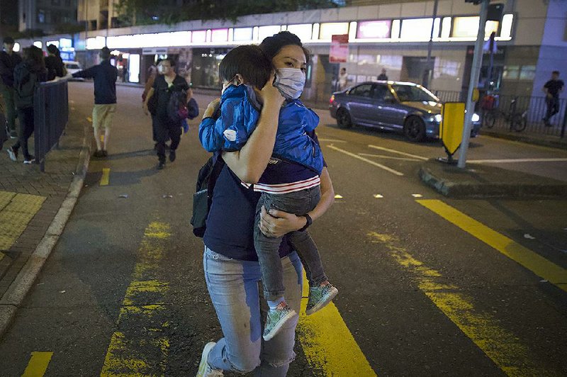 A woman carrying a child runs away Sunday as policemen con- front pro-democracy protesters on a Hong Kong street. More photos are available at arkansasonline.com/122hongkong/ 