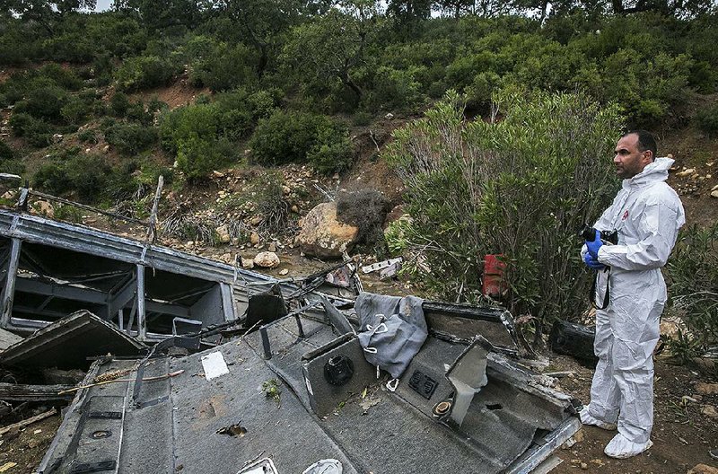 A police investigator stands by the wreckage of a regional bus that plunged from a hill Sunday, killing at least 24 passengers who were on an excursion in northern Tunisia’s Amdoun region. 