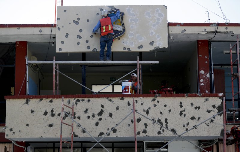 Workers repair the facade of City Hall riddled with bullet holes, in Villa Union, Mexico, Monday, Dec. 2, 2019. The small town near the U.S.-Mexico border began cleaning up Monday even as fear persisted after 22 people were killed in a weekend gun battle between a heavily armed drug cartel assault group and security forces. (AP Photo/Eduardo Verdugo)