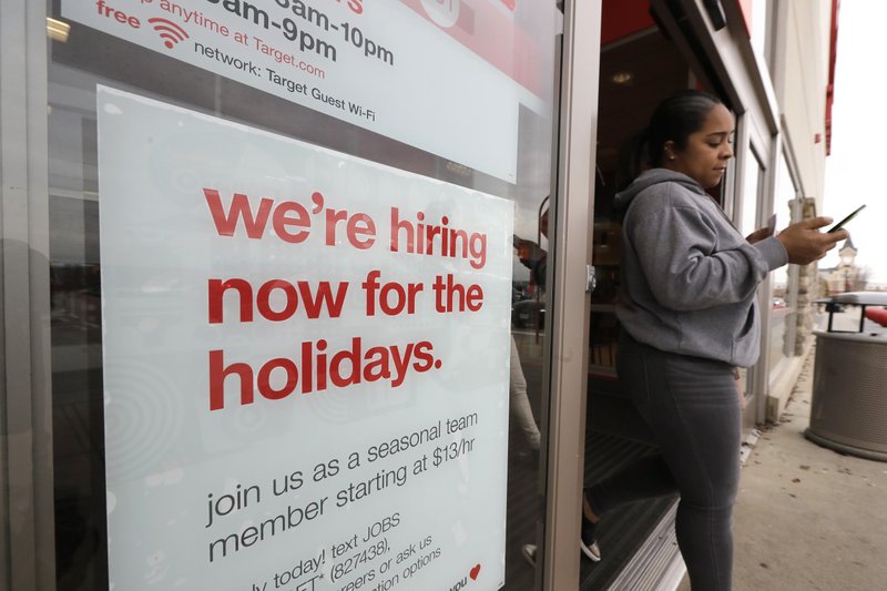 In this Nov. 27, 2019 photo a passer-by walks past a hiring for the holidays sign near an entrance to a Target store location, in Westwood, Mass.  (AP Photo/Steven Senne)