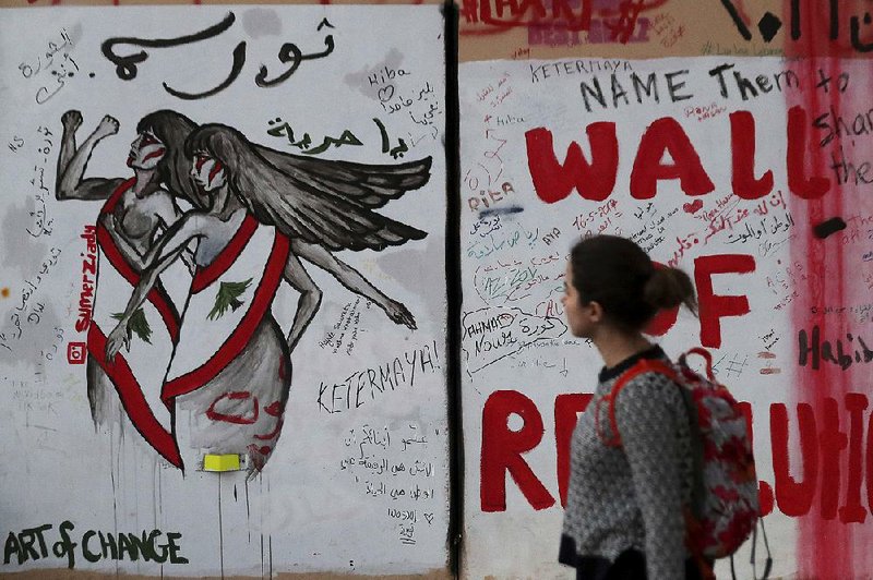 A woman looks at a wall decorated with graffiti in Arabic that reads, “Revolution is a woman, and Oh freedom,” during ongoing protests, in Beirut. Lebanon’s wave of anti-government protests has given a new platform for women struggling against religious laws. 