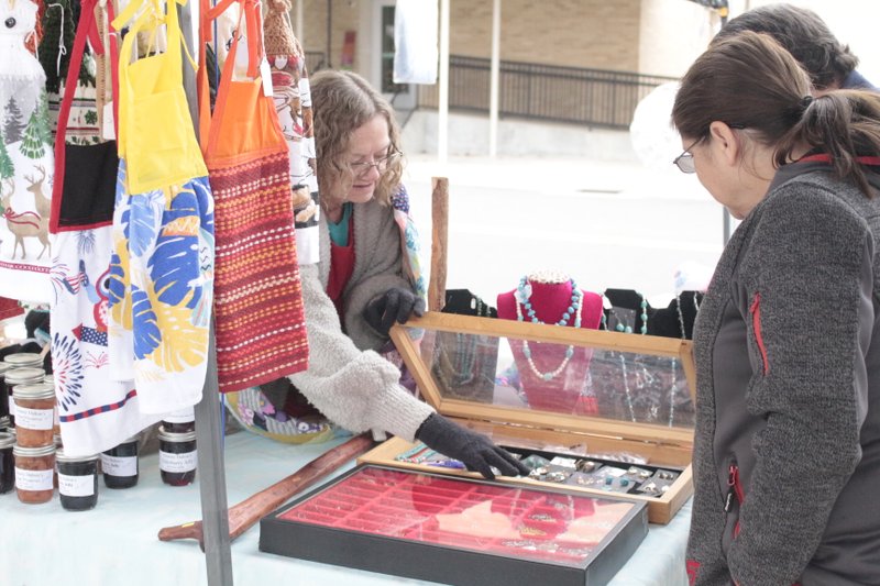 Krystal Whitecloud, left, holds open a display case full of Native American-style turquoise and silver jewelry for customers Cindy (forefront) and James Lindsay at Saturday’s second-annual MAD Holiday Market.
