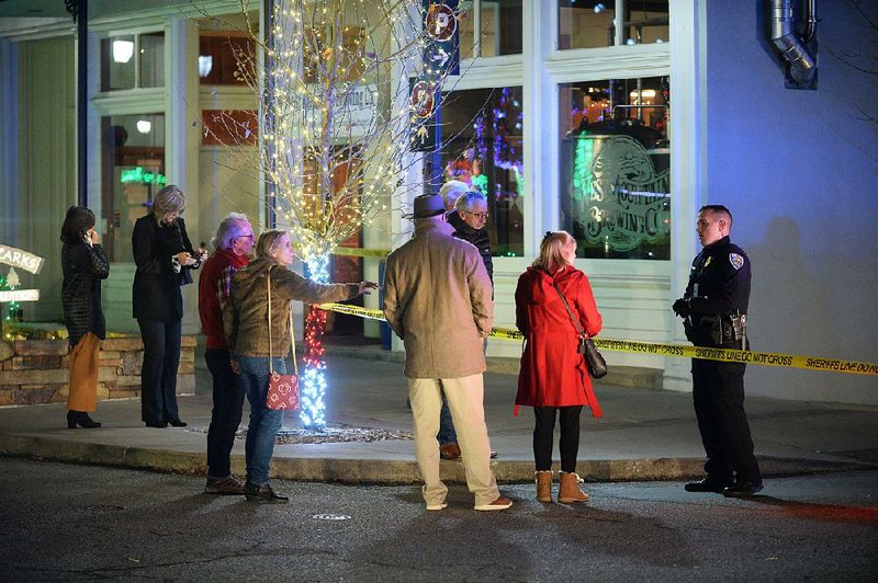 Bystanders ask a police officer about the shooting Saturday night outside the Fayetteville police station. Shots reportedly were heard by people attending the Lights of the Ozarks display on the Fayetteville town square.