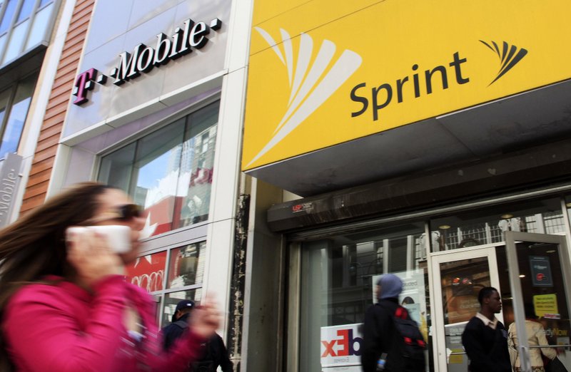 FILE - In this April 27, 2010 file photo, a woman using a cell phone walks past T-Mobile and Sprint stores in New York. T-Mobile, in its attempt to buy Sprint for $26.5 billion, shrinking the major wireless companies to three from four and creating another phone giant to rival AT&amp;T and Verizon, has already notched approvals from federal national-security, telecommunications and antitrust regulators. Now it must convince a federal court judge in New York that the 14 state attorneys general suing to stop its deal are wrong. (AP Photo/Mark Lennihan, File)