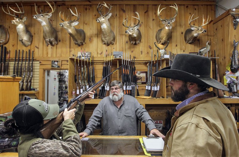 In this 2017 file photo, Jordan Pounders, from Pleasant Plains, left, looks down the barrel of a Browning Medallion rifle as she shops for a gun with her husband Logan Pounders at Ft. Thompson Sporting Goods in Sherwood. Big game hunter Jordy Oates, center, was helping recommend a weapon for Jordan to use for the first day Modern Gun Season for deer and bear hunters. Arkansas Democrat-Gazette/BENJAMIN KRAIN