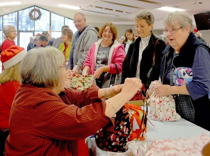 Keith Bryant/The Weekly Vista Volunteers, left, pass out cookies and gift wrap boxes for participants at last Saturday's Highlands Church Cookie Walk. Cookie Walk co-chair Sue LaHood said that volunteers had been working at the church all week, with a five-hour day being the shortest they put in. LaHood estimated volunteers baked between 14,000 and 20,000 cookies for the event, which raises money for mission trips, Gravette schools, Meals on Wheels and other programs.