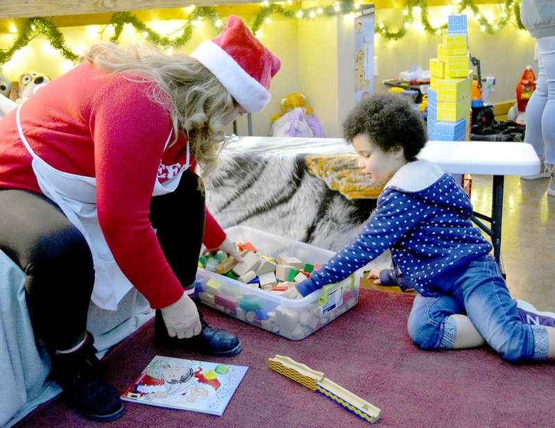 Keith Bryant/The Weekly Vista Kimi Henley (left), playing the storyteller in Santa's workshop, helps Yulissa Young, 4, select wooden blocks to play with while she waits in line to sit in Santa's lap.