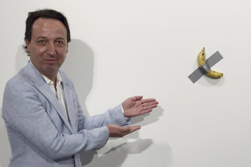 FILE- In this Dec. 4, 2019 photo, gallery owner Emmanuel Perrotin poses next to Italian artist Maurizio Cattlelan's &quot;Comedian&quot; at the Art Basel exhibition in Miami Beach, Fla. The work sold for $120,000. A Miami couple who bought a headline-grabbing banana duct-taped to a wall say they acknowledge the absurdity of the artwork, but believe it will become an icon and plan to gift it to a museum. (Siobhan Morrissey via AP)