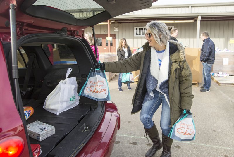 Kimberly Scott, volunteering with a group from Spin Master, adds a bag of supplies to a vehicle Friday during the annual Sharing &amp; Caring of Benton County distribution at the fairgrounds in Bentonville. About 300 volunteers were on hand when the gates opened at 7:30 a.m. to distribute clothing, presents and food to 3,460 children in need from Benton County, said Sarah Semrow, Sharing &amp; Caring executive director. Families apply for assistance in October and volunteers shop for each child's needs. Additional items, including household staples and school supplies, are handed out to each family as they drive through the distribution line. Go to nwaonline.com/photos to see more photos. NWA Democrat-Gazette/BEN GOFF &#8226; @NWABENGOFF