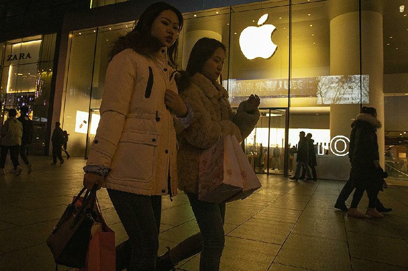 Shoppers walk past an Apple store Friday in Beijing. A new round of U.S. tariffs on a range of consumer items that China sells the U.S. has been called off under the first phase of the two nations’ trade deal.  