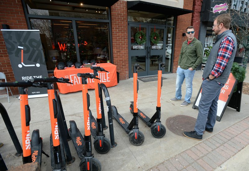 NWA Democrat-Gazette/ANDY SHUPE Daniel White (left), operations lead for Spin, speaks Friday with Brannon Pack, cycling coordinator for Experience Fayetteville, during a period of demonstration for the scooters introduced to the city Nov. 9.