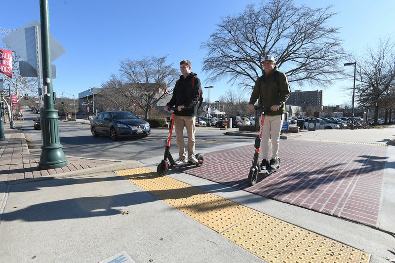 NWA Democrat-Gazette/J.T.WAMPLER Jack Seykora (left) and Gabe Hanna, both of Fayetteville, ride Spin scooters Thursday across Dickson Street. Seykora has used the scooters a few times and Hanna is a regular user with two or three trips a week. Spin has been operating around 200 e-scooters in the city and is permitted to have up to 250.