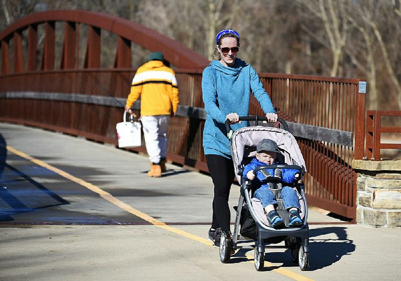 Anna Fendley walks Wednesday with her son, Declan, 1, on the Razorback Greenway near the Lake Springdale Trailhead. A study by a national market research and survey group found Northwest Arkansas residents like the trail systems, dislike driving during rush hours and want more and better public transit.