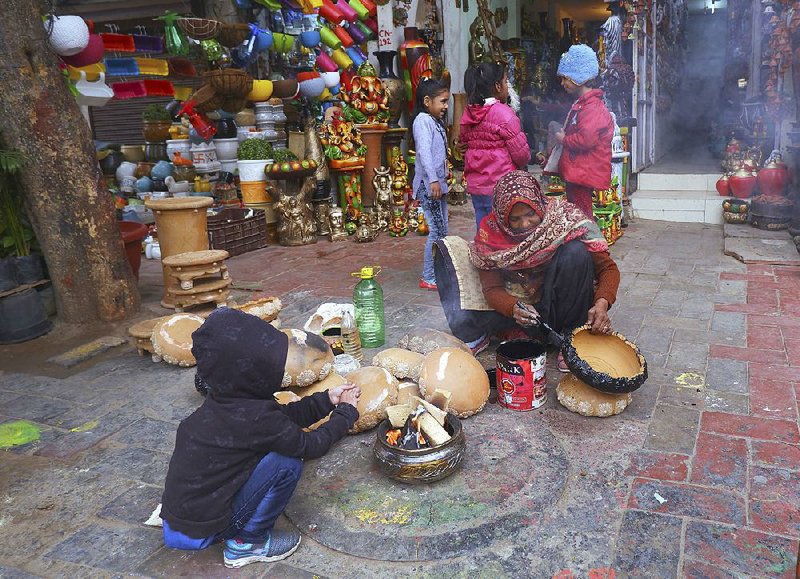 A potter paints as a child warms himself at a fire in New Delhi, where cold and foggy conditions continued Saturday. The temperature dipped into the mid-30s in India’s capital, and this December is expected to be the second-coldest there since 1901, weather officials say.  