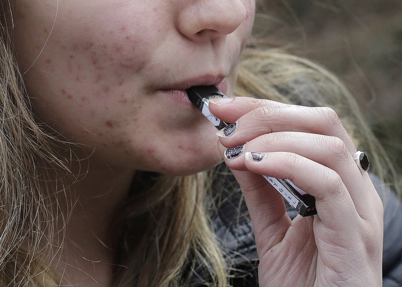 FILE - In this April 11, 2018, file photo, a high school student uses a vaping device near a school campus in Cambridge, Mass. The Trump administration announced Thursday that it will prohibit fruit, candy, mint and dessert flavors from small, cartridge-based e-cigarettes that are popular with high school students. But menthol and tobacco-flavored e-cigarettes will be allowed to remain on the market. (AP Photo/Steven Senne, File)

