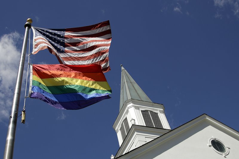 FILE - In this April 19, 2019, file photo, a gay pride rainbow flag flies along with the U.S. flag in front of the Asbury United Methodist Church in Prairie Village, Kan., United Methodist Church leaders are proposing creation of a separate division that would let more traditional denominations break away because of the disagreement with churches over the UMC&#x2019;s official stance on gay marriage. (AP Photo/Charlie Riedel, File)