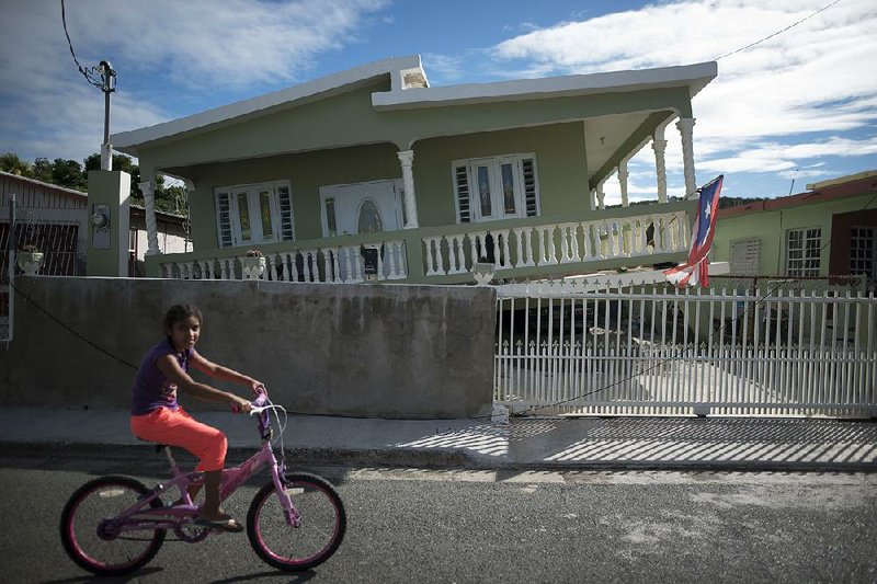 A girl rides her bicycle past a home that partially collapsed Monday in the earthquake that hit Guanica, Puerto Rico.