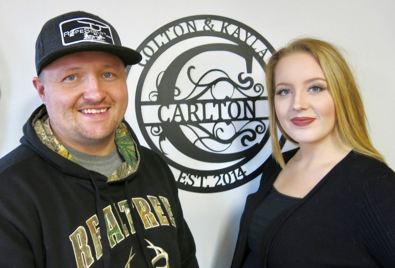 Westside Eagle Observer/SUSAN HOLLAND Colton and Kayla Carlton pose with one of the custom signs Colton produces in his shop at Weld Source Welding and Fabrication in Hiwasse. The Carltons opened the business Dec. 16 at 13781 Highway 72. Open hours are 8 a.m. to 5 p.m. Monday through Friday and 9 a.m. to 12 noon on Saturday. The business phone is 479-787-0336.