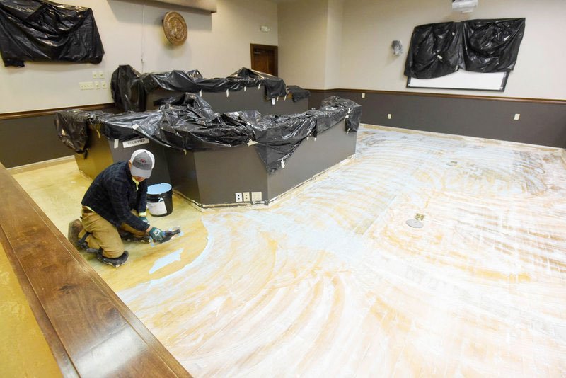 NWA Democrat-Gazette/FLIP PUTTHOFF Sam Bouphasiri spreads glue on the floor of a courtroom at the Benton County Courthouse annex to prepare it for carpet.