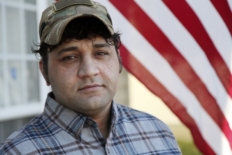 In this Monday, Dec. 16, 2019, photo, Zia Ghafoori stands beside an American flag hanging at his Charlotte, N.C., home. The Afghan interpreter spent 14 years working alongside U.S. Special Forces. He received a Special Immigrant Visa in 2014 and is working toward becoming a U.S. citizen. (AP Photo/ Sarah Blake Morgan)