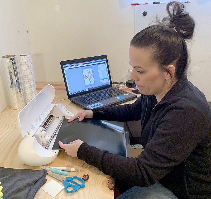 Sally Carroll/McDonald County Photo Krysti Sanny works with her computer and printer, readying to design and print a custom T-shirt. The home-based business in Goodman services the area with printed T-shirts, hoodies, banners, tumblers and more. Goodman Printing Company also ships orders across the country.