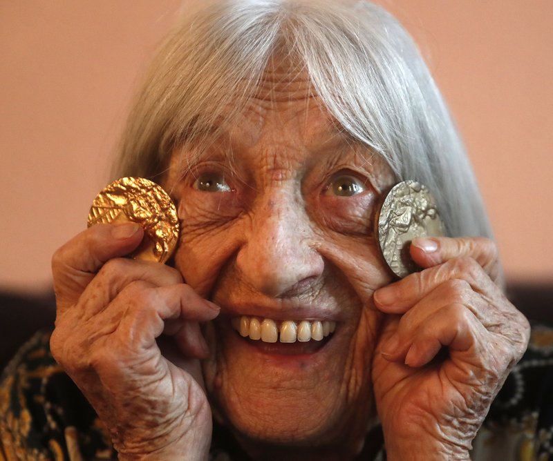 Agnes Keleti, former Olympic gold medal winning gymnast, poses for a photo with two of her Olympic medals at her apartment in Budapest, Hungary Wednesday Jan. 8, 2020. Although she turned 99 on Thursday, even a 9-year-old would have a hard time keeping up with Agnes Keleti's irrepressible energy and enthusiasm. Keleti is the oldest living Olympic champion and a Holocaust survivor. She won 10 medals in gymnastics &#x2014; including five golds &#x2014; at the 1952 Helsinki Games and at the 1956 Melbourne Games. (AP Photo/Laszlo Balogh)