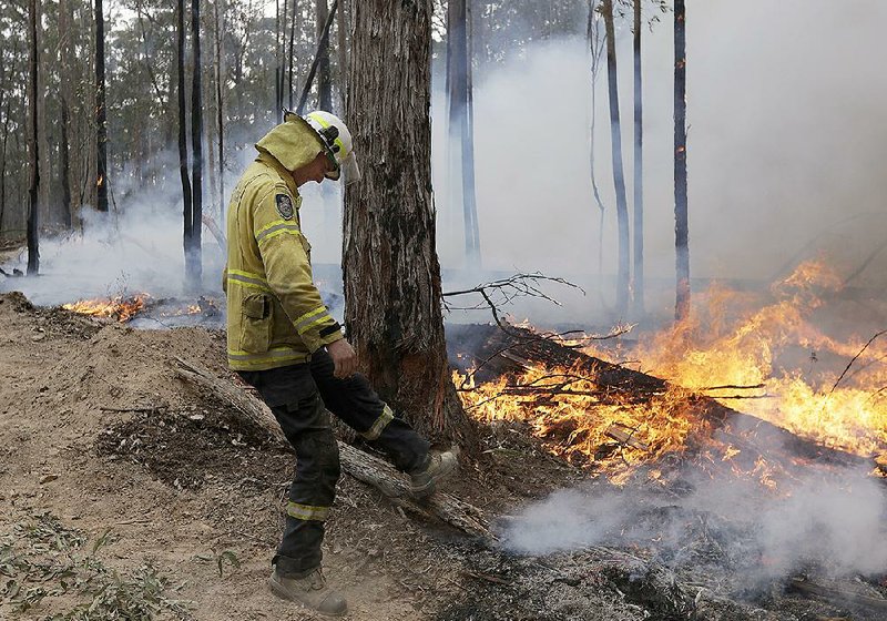 A firefighter kicks at a log Sunday while helping to build a fire-containment line near Bodalla, Australia. More photos at arkansasonline.com/113bodalla/.  