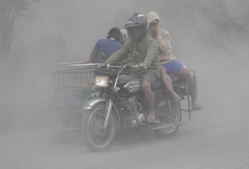 A family rides their motorcycle through clouds of ash as they evacuate to safer grounds as Taal volcano in Tagaytay, Cavite province, southern Philippines on Monday, Jan. 13, 2020. Red-hot lava is gushing from the volcano after a sudden eruption of ash and steam that forced residents to flee and shut down Manila's airport, offices and schools. (AP Photo/Aaron Favila)