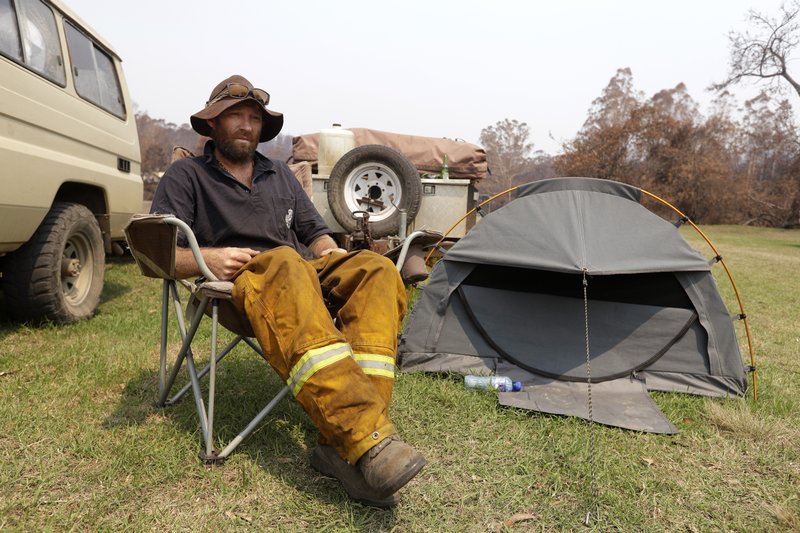 Volunteer firefighter Ash Graham camps on the lawn near the fire station at Nerrigundah, Australia, Monday, Jan. 13, 2020, since losing his house and his dog when a wildfire ripped through the town on New Year's Eve. The tiny village of Nerrigundah in New South Wales has been among the hardest hit by Australia's devastating wildfires, with about two thirds of the homes destroyed and a 71-year-old man killed. (AP Photo/Rick Rycroft)