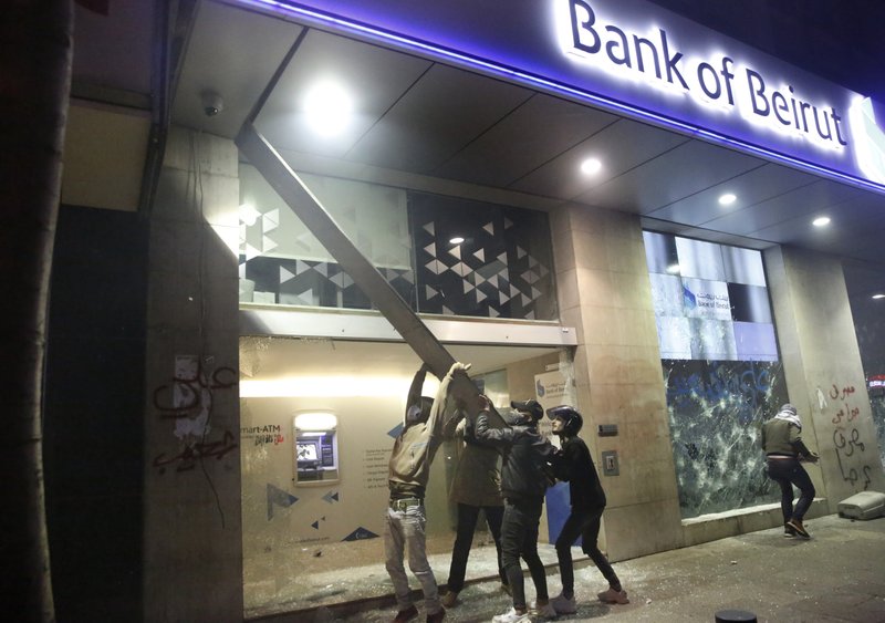 Anti-government protesters break a bank security camera as other smashes the widows, during ongoing protests against the Lebanese central bank's governor and against the deepening financial crisis, at Hamra trade street, in Beirut, Lebanon, Tuesday, Jan. 14, 2020. Lebanese security forces lobbed tear gas at protesters who responded with rocks outside the country's central bank Tuesday, a violent turn after demonstrators returned to the streets following a weekslong lull. (AP Photo/Hussein Malla)