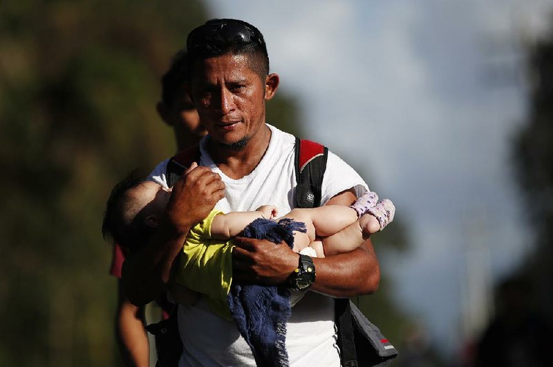 Honduran migrant Selvin Hernandez carries the daughter of another migrant Wednesday as a group trying to get to the United States passes near El Cinchado, Guatemala. More photos at arkansasonline.com/116venezuela/.
(AP/Moises Castillo)