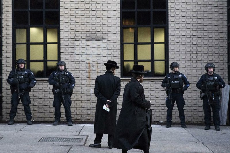 Orthodox Jewish men pass New York police guarding a Brooklyn synagogue prior to a funeral for Mosche Deutsch, a rabbinical student from Brooklyn who was killed in a shooting at a Jersey City, N.J., market. A group of security experts recommended that Jewish congregations opting to deploy armed security personnel use uniformed law enforcement officers rather than private guards or volunteers from the community.
(AP/Mark Lennihan)