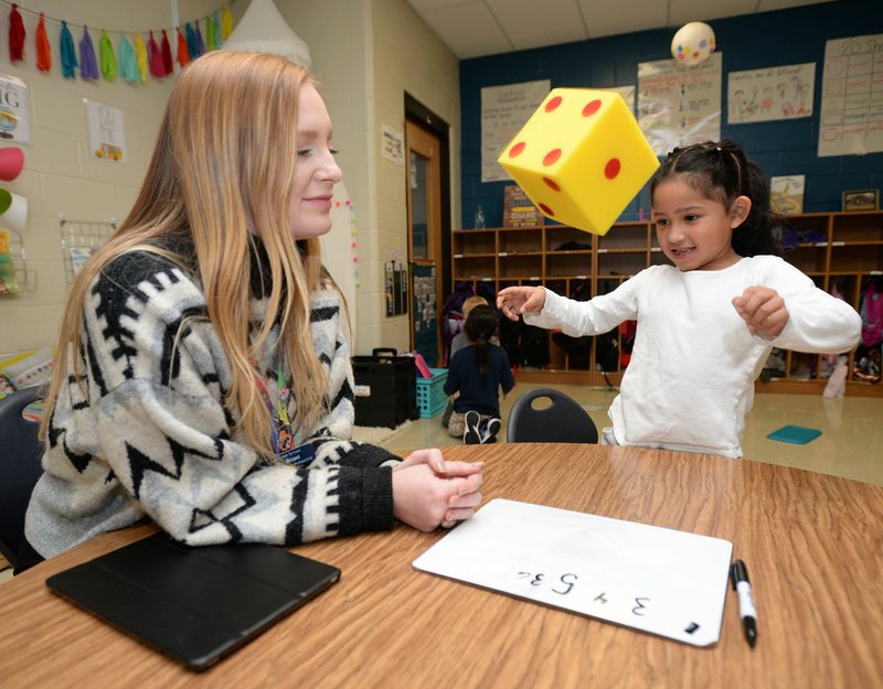 Madison Weast (left), a kindergarten paraprofessional, watches Thursday as Kimberly Diaz-Hernandez, 6, tosses a die during math instruction in Kodi Murphree's kindergarten class at Owl Creek School in Fayetteville. The Fayetteville School Board is considering moving Asbell Elementary and Owl Creek schools to the traditional calendar next school year. Go to nwaonline.com/200124Daily/ for today's photo gallery. (NWA Democrat-Gazette/Andy Shupe)