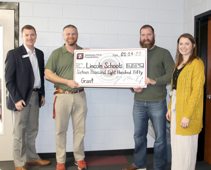 John Morris (left) and Megan Hudgens (right) both with Simmons Bank, present a ceremonial check to Ivan Huffmaster and Stan Karber with Lincoln Middle School. The grant from Simmons First Foundation will be used to build an outdoor adventure park next to the school. (NWA Democrat-Gazette/Lynn Kutter)