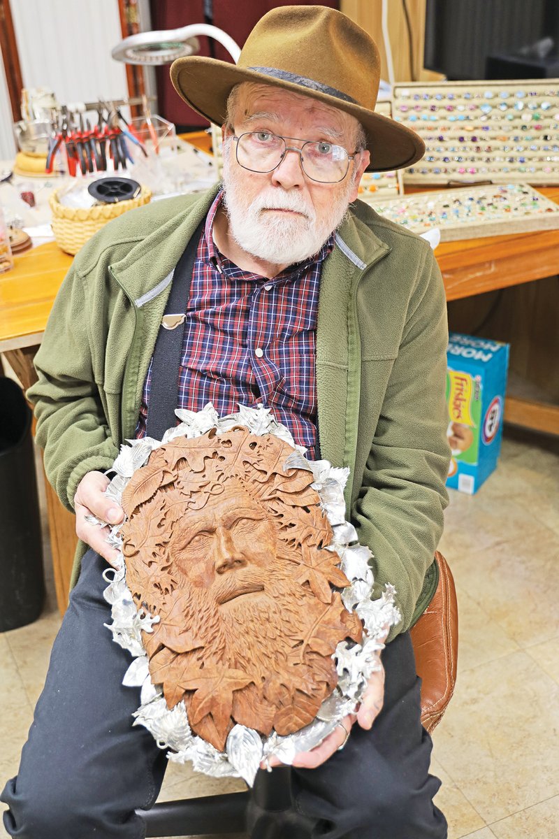 Charles Widmer holds a carved wood self-portrait, surrounded by metal leaves. During his career as a woodcarver, he completed hundreds of art pieces, including a massive eagle for President Jimmy Carter’s presidential library.