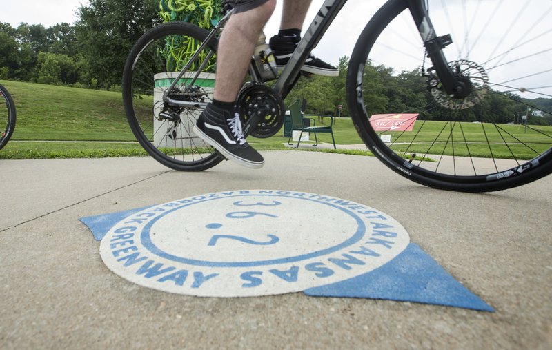 In this  June 22, 2019 file photo, a cyclist passes a Razorback Regional Greenway mile marker on the Lake Bella Vista trail in Bentonville.