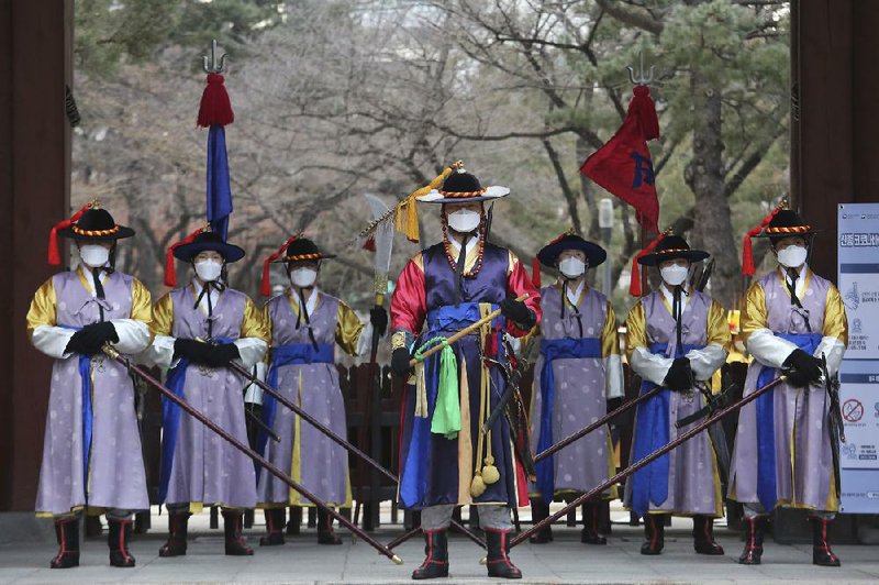 South Korean imperial guards take precautions against the coronavirus outbreak Thursday during a reenactment of the Royal Guards Changing Ceremony outside Deoksu Palace in Seoul. South Korea confirmed its first case of person-to-person spread of the virus Thursday.