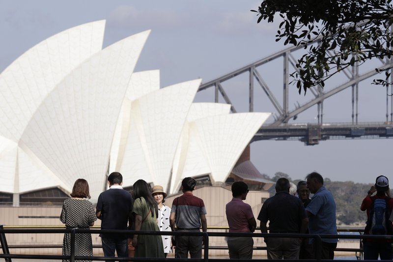 In this Jan. 22, 2020, photo, tourists gather to have their photos taken with the Opera House and Harbour Bridge as a backdrop in Sydney, Australia. Tourism Australia, a government agency tasked with promoting the country overseas, has taken steps to counter mainstream media messages that Australia is a nation on fire, pointing out that many tourist attractions have not been affected by the crisis. (AP Photo/Rick Rycroft)