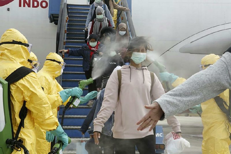 Indonesians arriving from Wuhan, China, are sprayed with antiseptic Sunday at Hang Nadim Airport in Batam, Indonesia. Travelers who were evacuated from Wuhan, the Chinese city at the center of the coronavirus outbreak, were moved to a quarantine zone. More photos at arkansasonline.com/23outbreak/. 